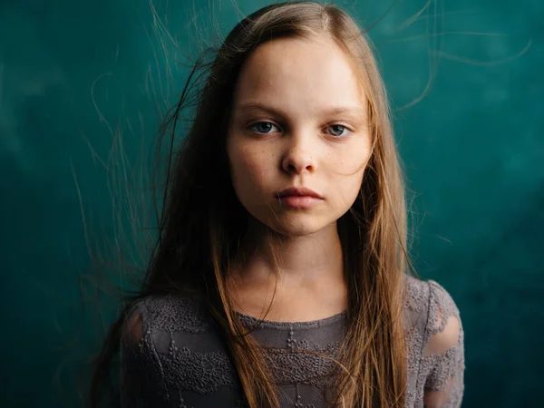 Sad girl with disheveled hair on a turquoise background in a gray dress — ストック写真