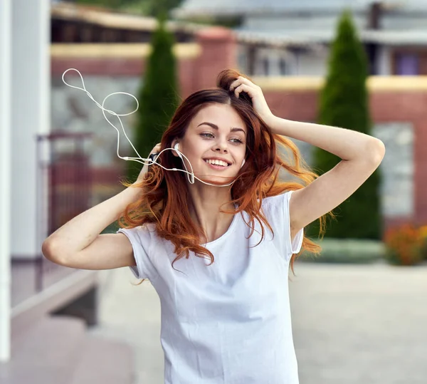 Mooie vrouw in wit t-shirt lopen door de straat leuke vrijetijdsmuziek met hoofdtelefoon — Stockfoto
