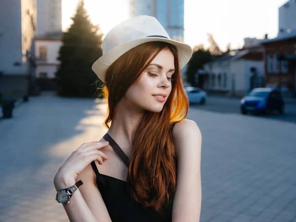 Красивая женщина с рыжими волосами в белой шляпе и в черном платье на улице в городе — стоковое фото
