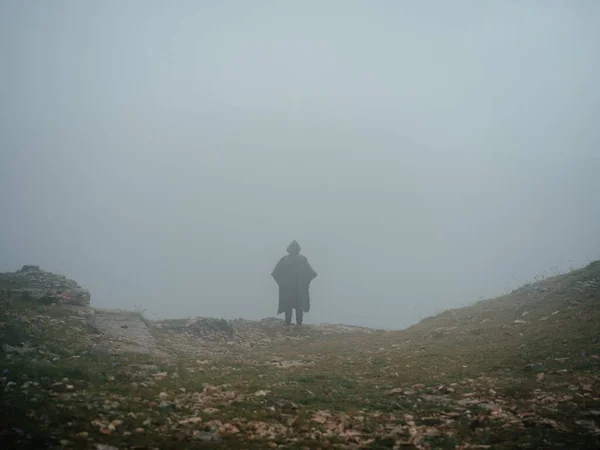 Un hombre camina en la naturaleza en las montañas con un abrigo negro y una capucha —  Fotos de Stock