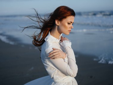 Okyanus kıyısında kumların üzerinde beyaz elbiseli bir kadın.