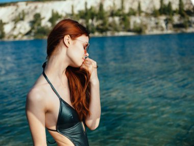 Doğada şeffaf bir nehrin kenarında yeşil mayo ve gözlüklü seksi bir kadın.