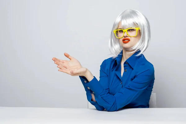 Элегантная женщина в белом парике сидит за столом в желтых очках и жестикулирует эмоциями рук — стоковое фото