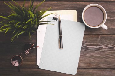 Masanın üzerinde beyaz bir fincan kahve, not defteri ve ofis kırtasiyesi.