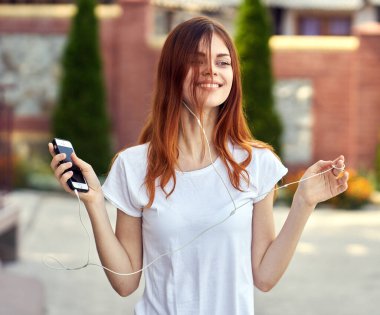 Beyaz tişörtlü bir kadın sokak müziğinde kulaklık takıyor.