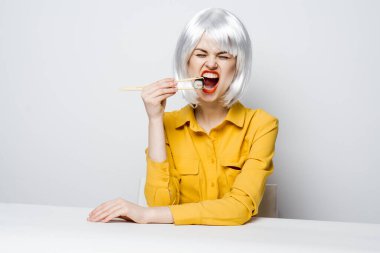 Yemek çubukları ile neşeli sarışın masada oturmuş suşi yiyor.