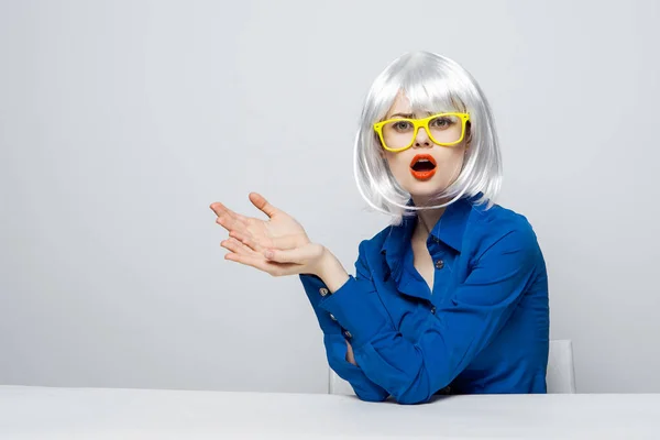 Mulher elegante em uma peruca branca senta-se a uma mesa em óculos amarelos e gestos com suas emoções de mão — Fotografia de Stock