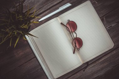 Kalem ve ofis gözlüklü not defterini aç. Cep telefonu çiçeği bir kap üst görünümde iç görünümde.