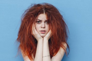 Mavi arka plandaki dağınık saçlı kadın saç modelini bitiriyor.