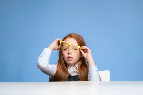 Vörös hajú lány sárga szemüveggel ül az asztalnál érzelmek oktatás — Stock Fotó