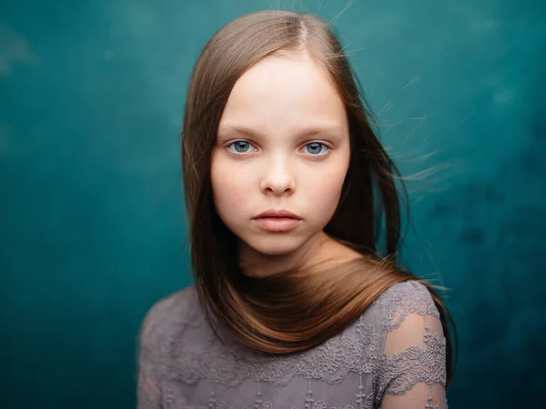 Gyönyörű kislány egy szürke ruha közelkép vágott kilátás szőke haj türkiz háttér — Stock Fotó
