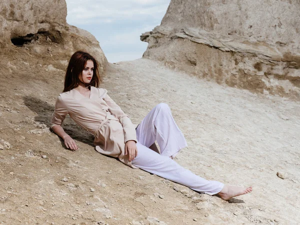 Een mooie vrouw in lichte kleren ligt op het zand in de rotsen voor de natuur — Stockfoto