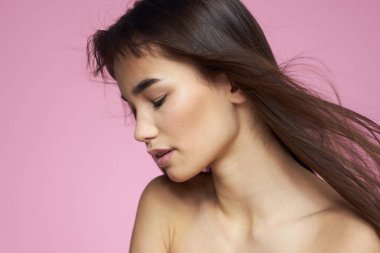 Güzel esmer, çıplak omuzlar, açık pembe arka plan.