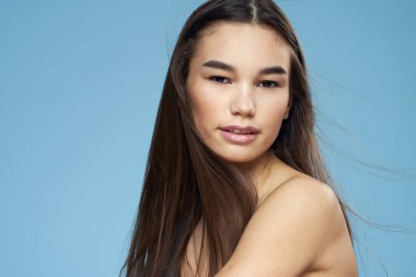 Güzel esmer, çıplak omuzlar uzun saç bakımı mavi arka plan