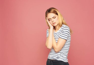 Pembe arka planda çizgili tişörtlü üzgün sarışın kadın.