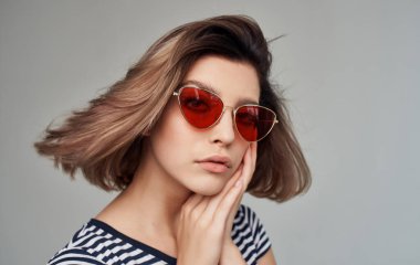 Gri arka planda çizgili tişörtlü romantik kadın portresi ve yüzünde şık gözlükler.