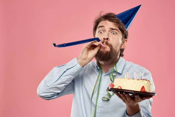 髭を生やした男とケーキの舌でピンクの背景クロップドビューと彼の頭の上にブルーキャップ — ストック写真