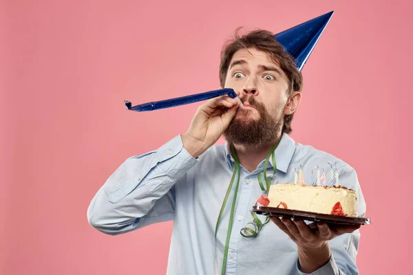 Baard man met taart tong op een roze achtergrond bijgesneden uitzicht en een blauwe dop op zijn hoofd — Stockfoto