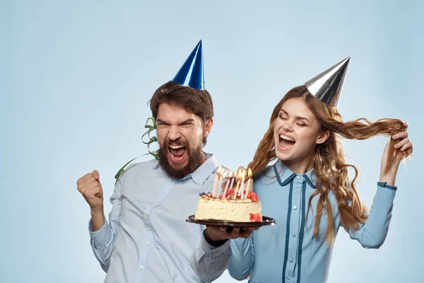 Мужчина и женщина празднуют день рождения с тортом и в шляпах на синем фоне — стоковое фото