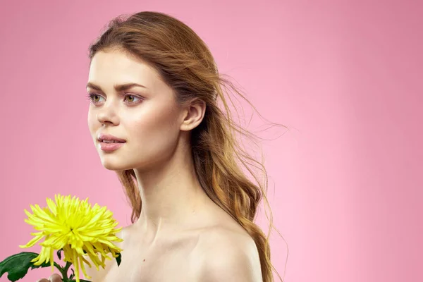 Piękna dziewczyna z żółtym kwiatem na różowym tle nagie ramiona makijaż — Zdjęcie stockowe