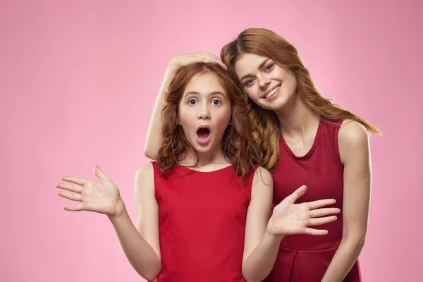 Mãe alegre e filha vestindo vestidos vermelhos estão de pé ao lado da família alegria no fundo rosa — Fotografia de Stock