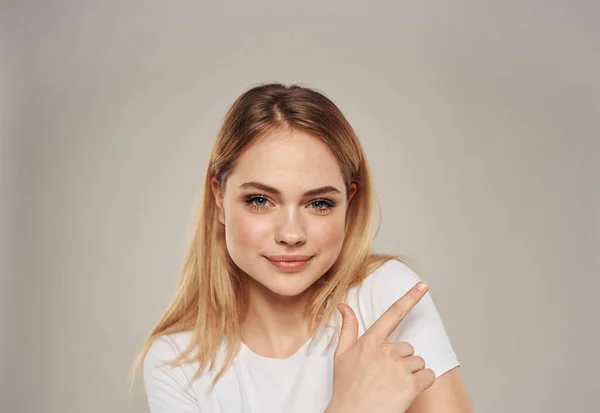 Copiar espaço mulher loira mostra sua mão para o lado em um fundo bege em uma camiseta branca — Fotografia de Stock