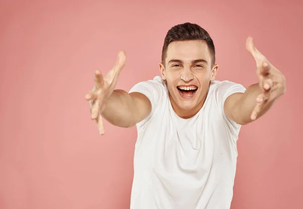 Hombre emocional en camiseta blanca gesto con las manos recortadas ver fondo rosa —  Fotos de Stock