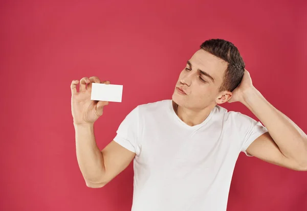 Pracovník s kreditní kartou na červeném pozadí a bílým tričkem oříznutý pohled — Stock fotografie