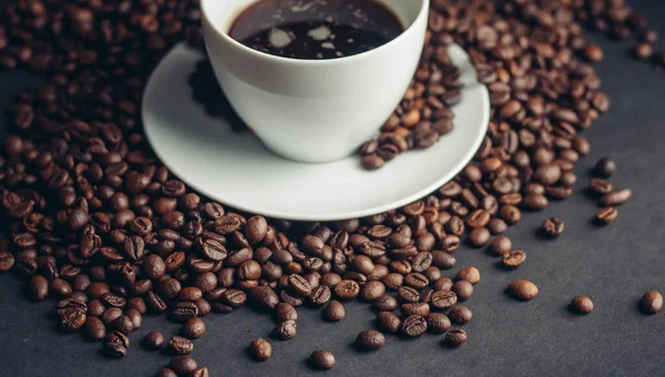 Ziarna kawy i filiżanka na białym spodku ciemne tło napój — Zdjęcie stockowe