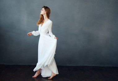 Beyaz elbiseli romantik bir kadın gri arka planda dans ediyor.