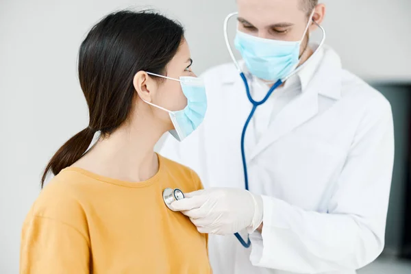 청진기를 가지고 있는 의사는 병원에서 의료용 마스크를 쓰고 있는 환자의 심장 박동 소리를 듣는다 — 스톡 사진