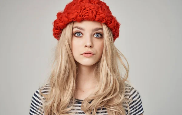 Beautiful blonde in a warm hat and striped T-shirt on a light background — Stock Photo, Image