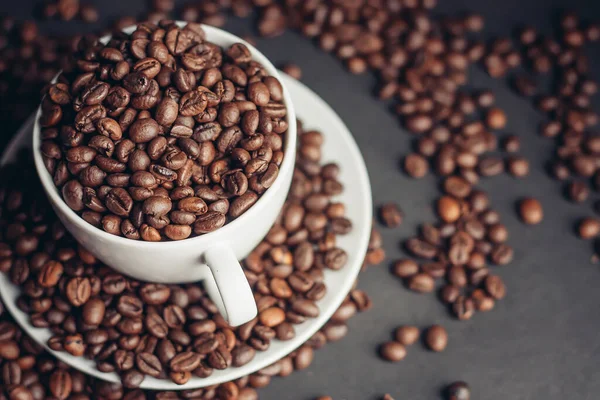 Una taza con granos de café se coloca en un platillo sobre un fondo gris de cerca — Foto de Stock