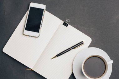 Masanın üzerinde kahve fincanı ve kalem telefon teknolojisi var.