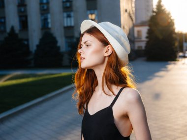 Siyah elbiseli ve beyaz şapkalı bir kadın portresi. Gün batımında binanın yanındaki sokakta.