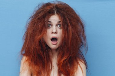 Üzgün kızıl saçlı, mavi arka planda dağınık saçlı, elleriyle el kol hareketi yapan bir kadın.