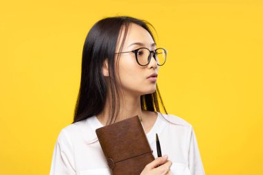 Gözlüklü bir iş kadını elinde not defteri ile resmi sarı izole bir arka plan tutuyor.