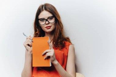 Elinde not defteri olan turuncu elbiseli bir kadın hafif arka planda bir bayan öğrenci eğitimi bilimi öğrencisi.