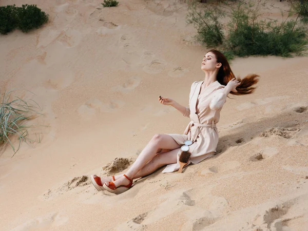 Una mujer en un vestido ligero y sandalias rojas en la arena en la playa cerca del mar —  Fotos de Stock