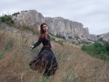 Siyah elbiseli romantik kadın dağlarda dinleniyor.