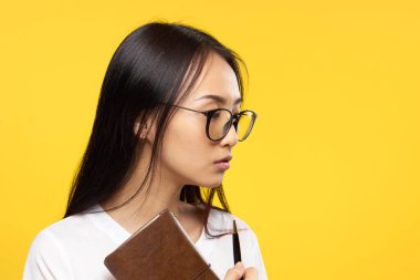 Beyaz tişörtlü güzel esmer kalem ofis sarı arka planlı not defteri tutuyor.