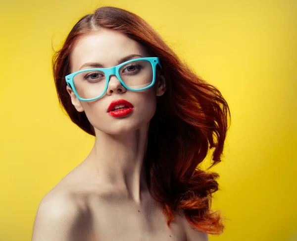 Pretty woman naked shoulders red lips blue glasses yellow background — Stock Photo, Image