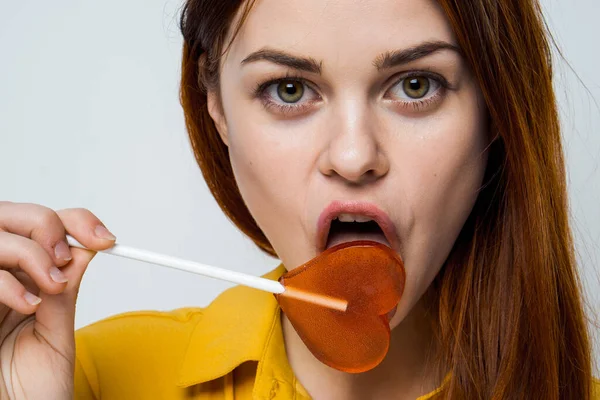 Attractive woman licking heart lollipop close-up studio — Stock Photo, Image