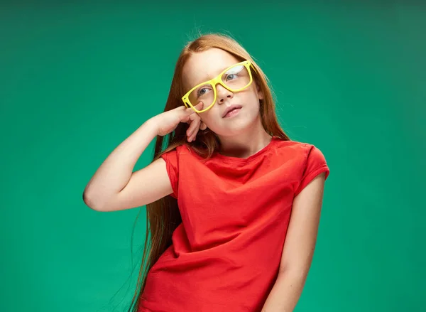 Χαριτωμένο κορίτσι κόκκινα μαλλιά gesturing με τα χέρια της παιδική ηλικία πράσινο σχολείο υποβάθρου — Φωτογραφία Αρχείου