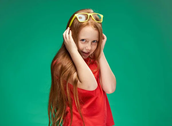 Mignonne fille aux cheveux roux avec des lunettes sur sa tête t-shirt rouge Studio fond vert — Photo