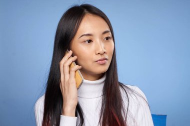Güzel esmer telefonda konuşuyor beyaz kazak teknolojisi mavi arka plan