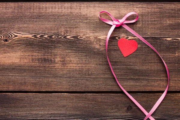 Lazo de cinta rosa y corazón rojo en una mesa de madera — Foto de Stock
