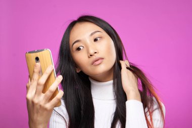 Neşeli, güzel esmer, elinde telefonla internet teknolojisi pembe arka planda.
