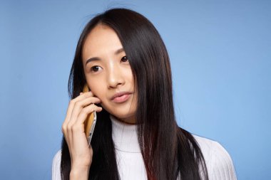 Güzel Asyalı kadın telefon teknolojisiyle konuşuyor mavi arka plan