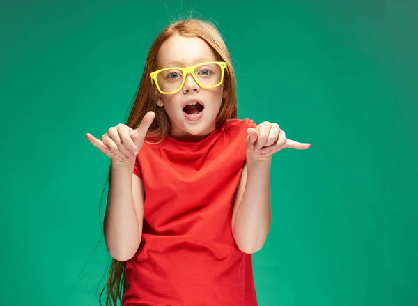 Linda chica de pelo rojo gesto con sus manos infancia verde fondo escuela —  Fotos de Stock